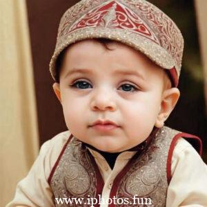 A baby wearing a white headscarf and necklace, looking adorable and innocent